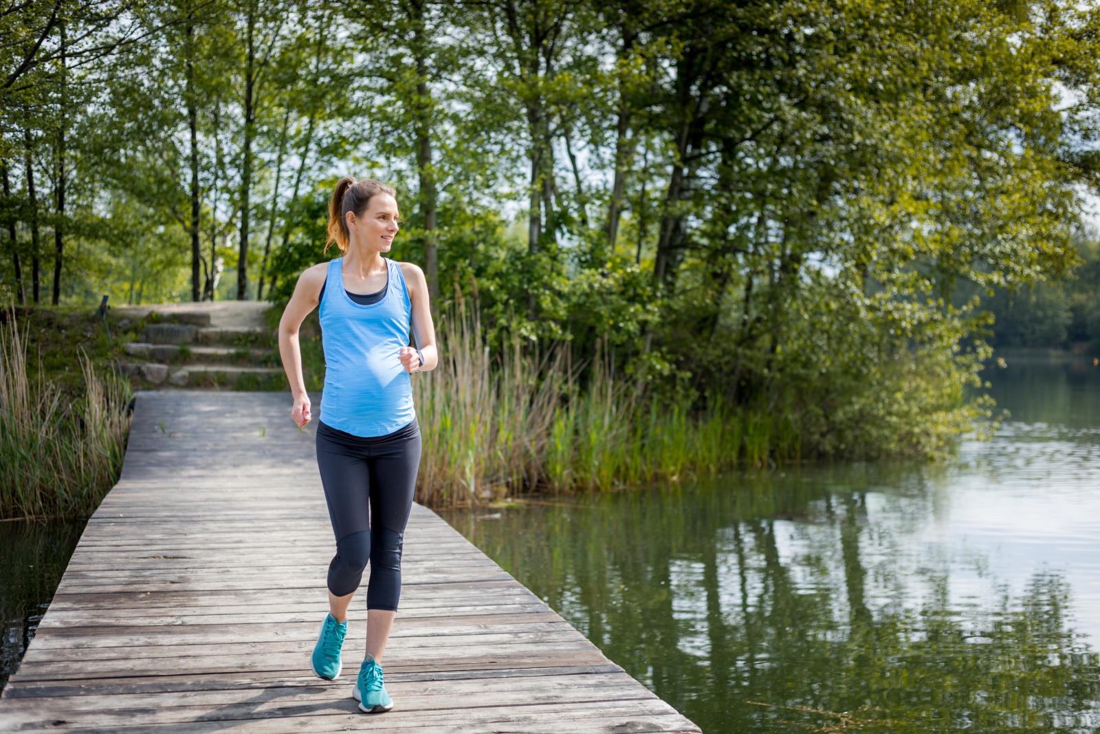 woman with visible pregnancy belly jogging in athletic gear outdoors across wooden boardwalk on lake